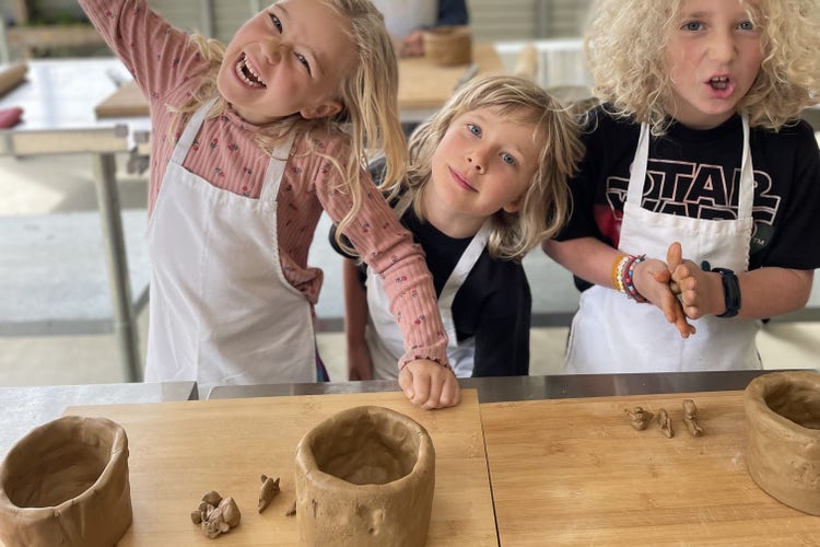 three children wearing aprons making pottery